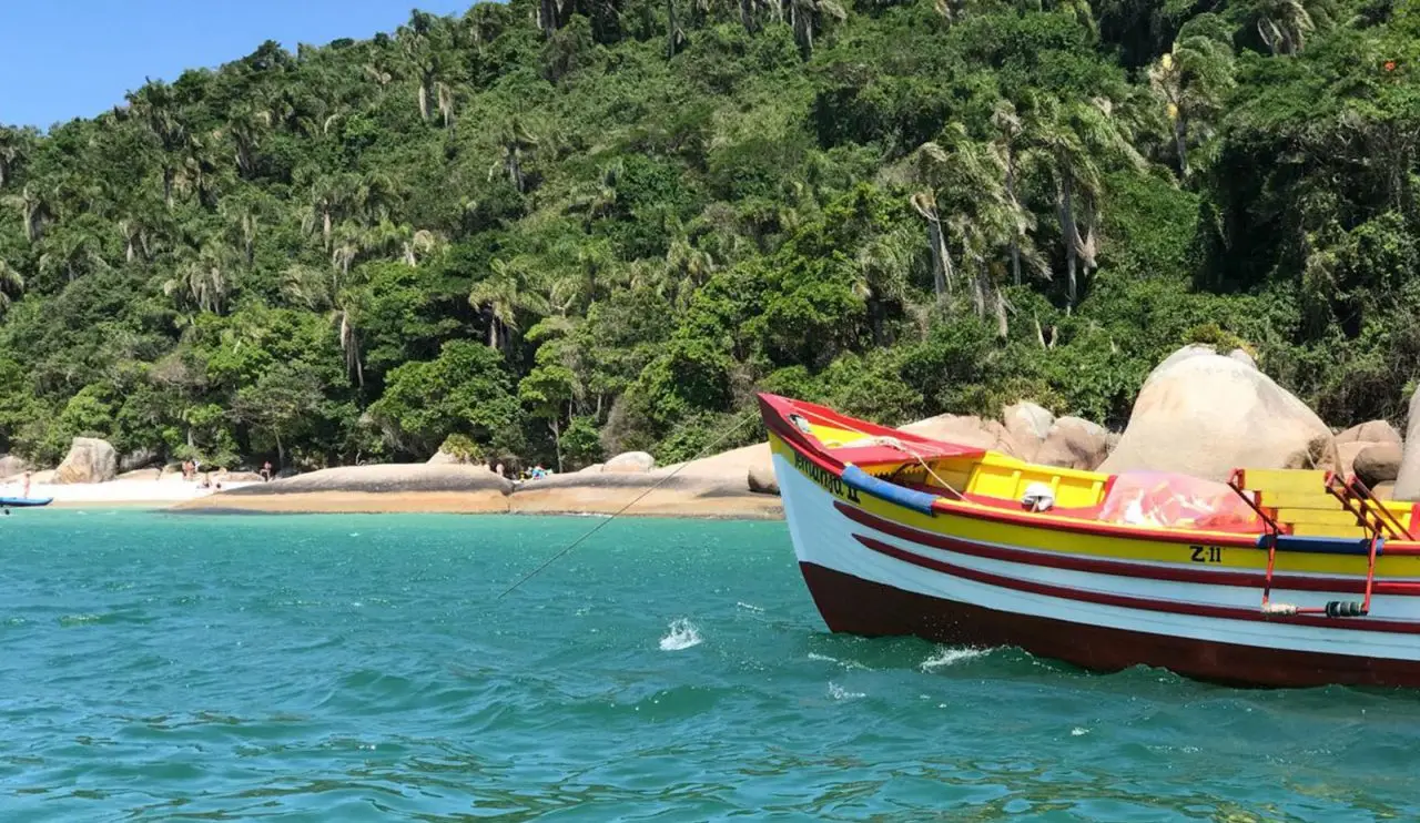 Dia lindo de sol com mar verdinho e barco na beira da praia na Ilha do Campeche em Florianópolis, Santa Catarina